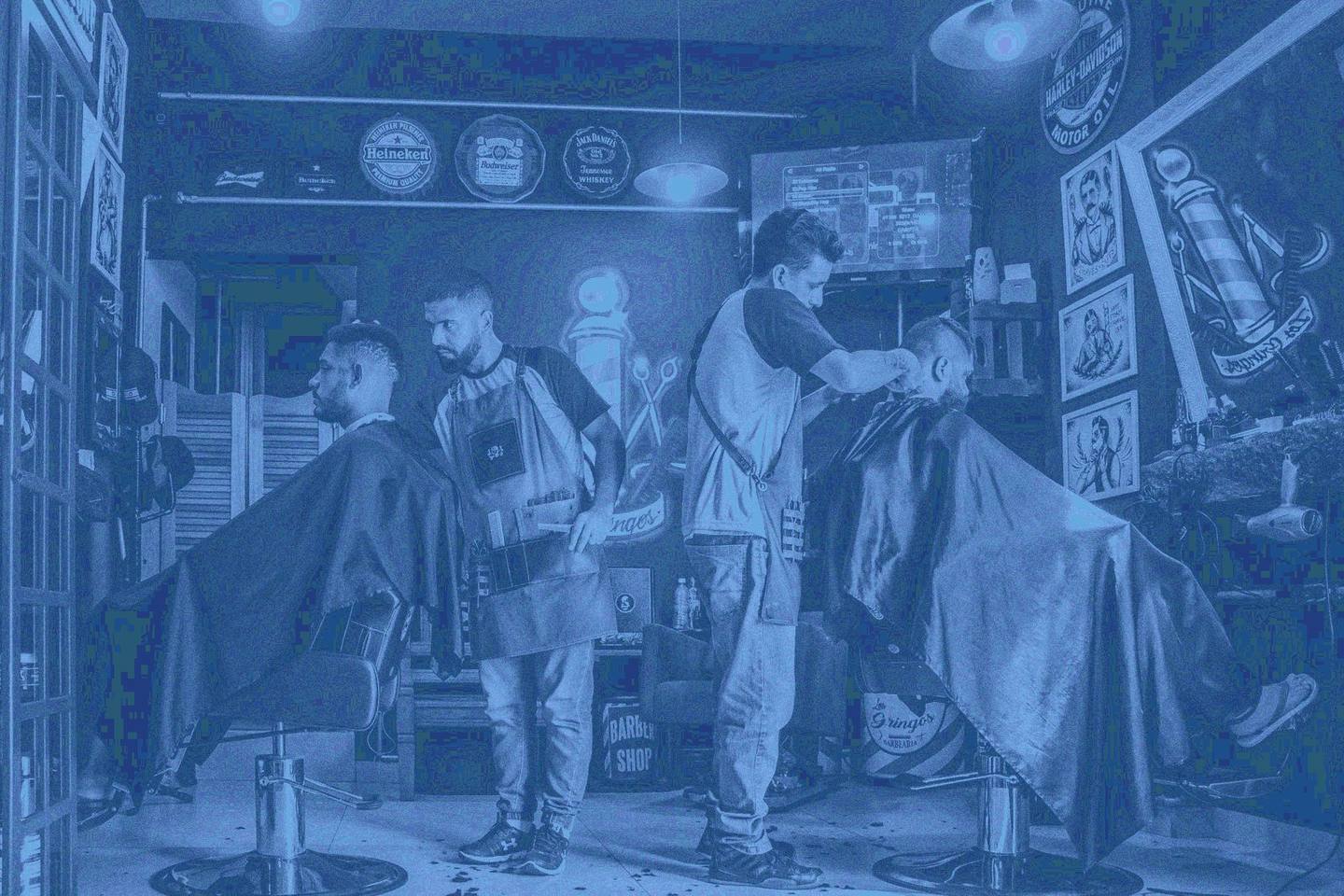 Inside a working barbershop, barbers cutting hair at their chairs